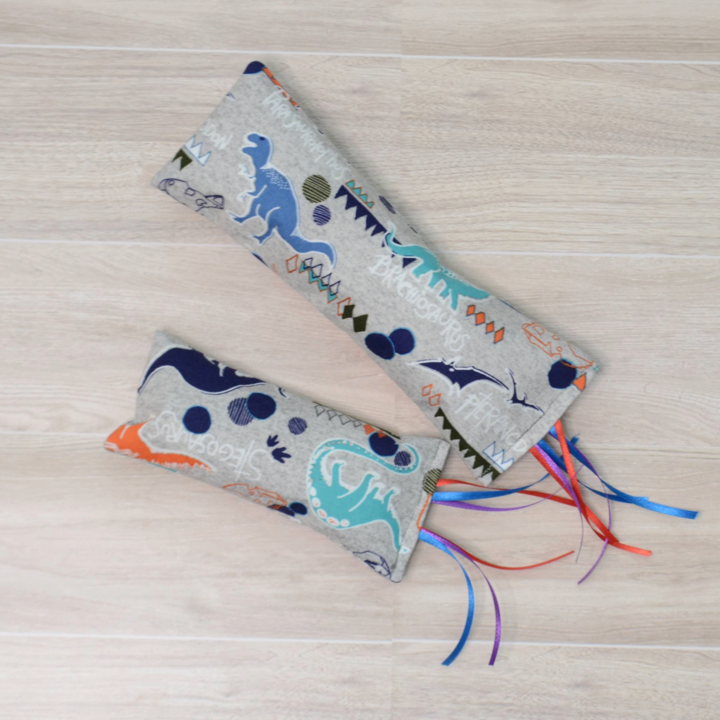 Two different sizes Kitty Kicker toy with dinosaur design and colorful ribbon on a wooden surface