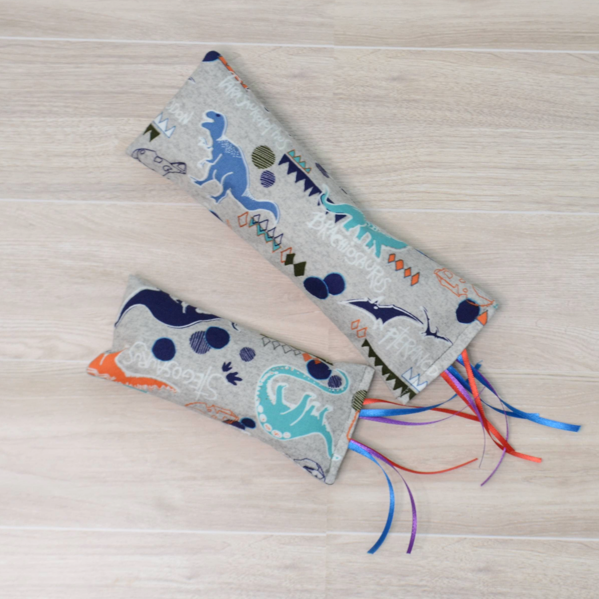 Two different sizes Kitty Kicker toy with dinosaur design and colorful ribbon on a wooden surface
