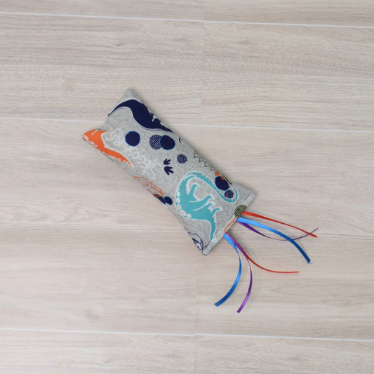 Kitty Kicker toy with dinosaur design and colorful ribbon on a wooden surface