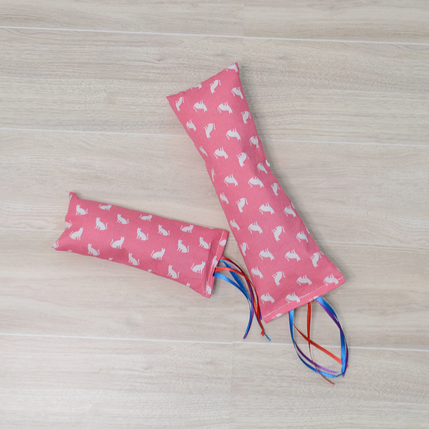 Two sizes Pink Kitty Kicker toy with white cat design and colorful ribbon on a wooden surface