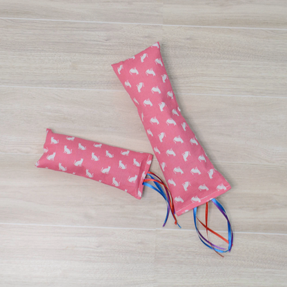 Two sizes Pink Kitty Kicker toy with white cat design and colorful ribbon on a wooden surface