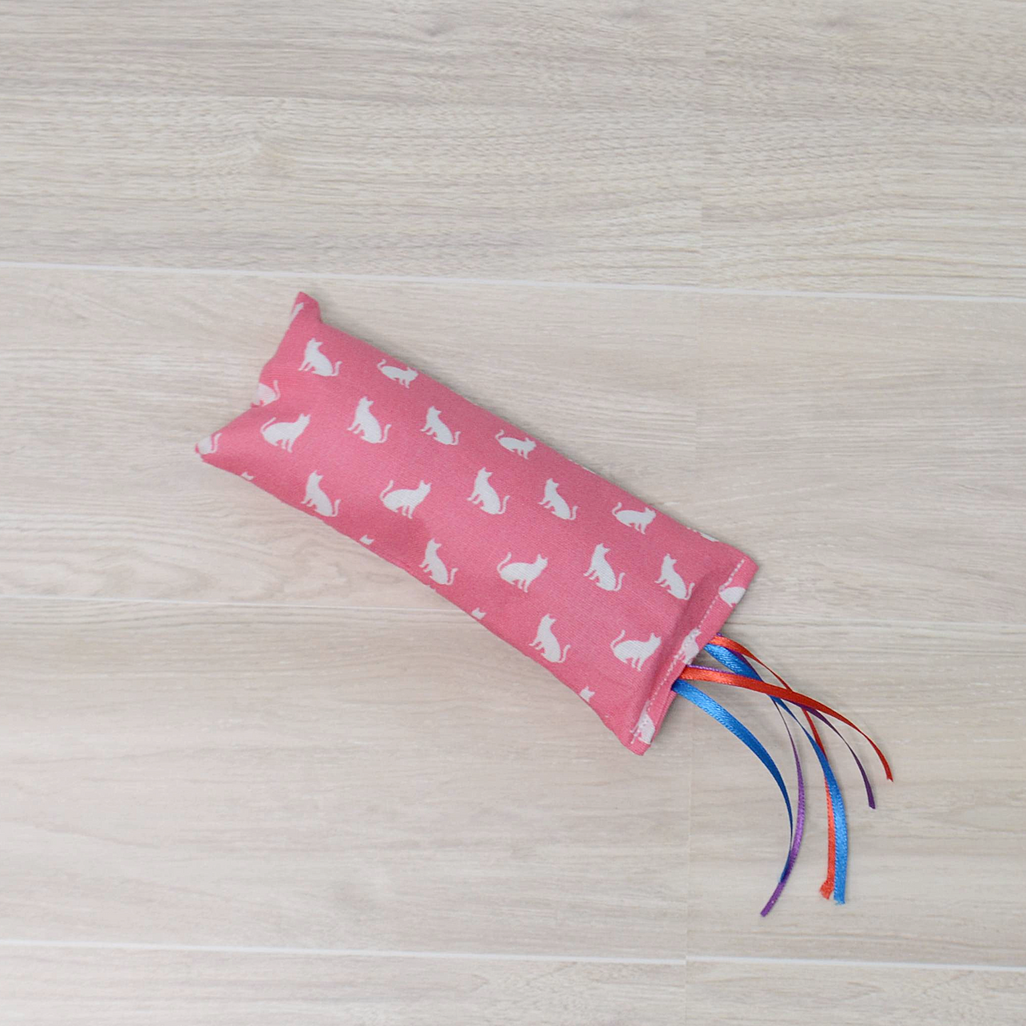 Pink Kitty Kicker toy with white cat design and colorful ribbon on a wooden surface