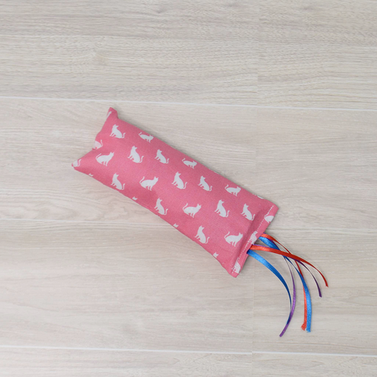 Pink Kitty Kicker toy with white cat design and colorful ribbon on a wooden surface