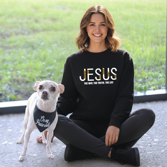 Woman wearing a black sweatshirt with 'JESUS' printed on it, sitting outdoors with a small dog.