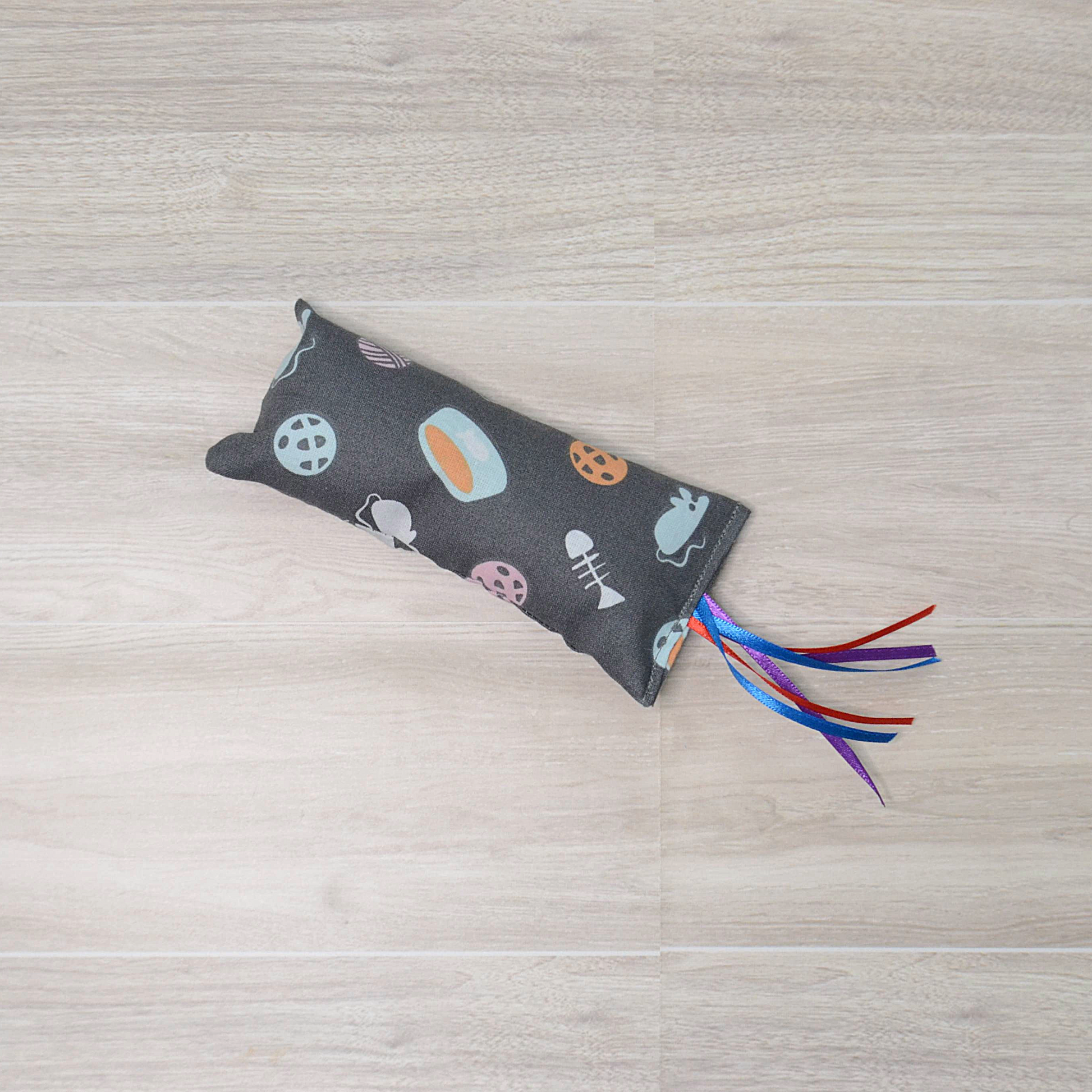 Gray Kitty Kicker toy with mouse and fish  design and colorful ribbon on a wooden surface