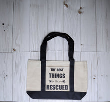 Load image into Gallery viewer, Cotton canvas tote bag with black straps. Design reads &quot;The best things in life are rescued&quot; with two paw prints
